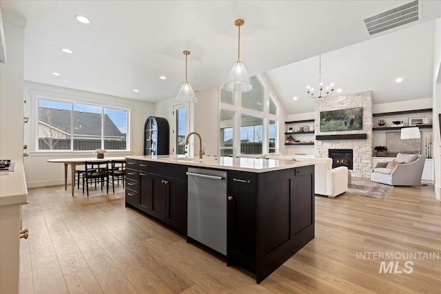 kitchen with dishwasher, a center island with sink, light hardwood / wood-style floors, pendant lighting, and a fireplace