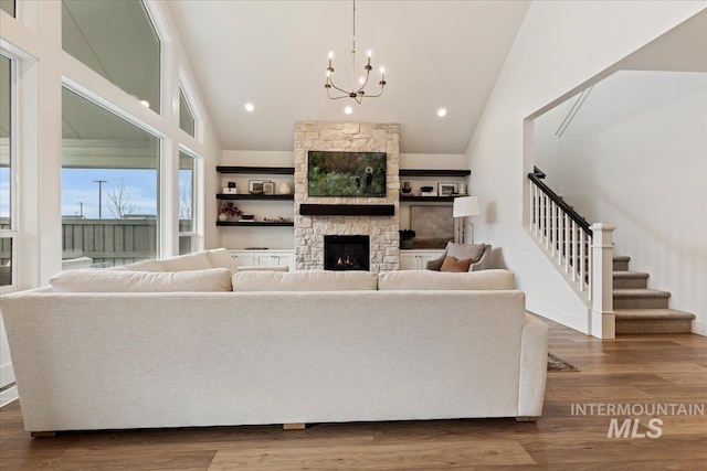 living room with a notable chandelier, a stone fireplace, high vaulted ceiling, and hardwood / wood-style flooring