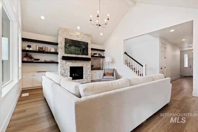 living room featuring a fireplace, vaulted ceiling with beams, a notable chandelier, and light hardwood / wood-style flooring