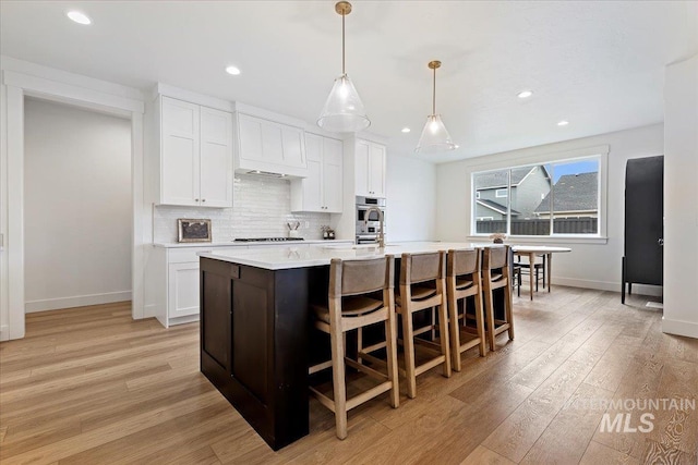 kitchen with light hardwood / wood-style flooring, decorative light fixtures, a center island with sink, stovetop, and white cabinetry