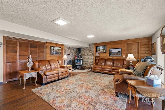 living room with a wood stove, a textured ceiling, dark hardwood / wood-style flooring, and wooden walls