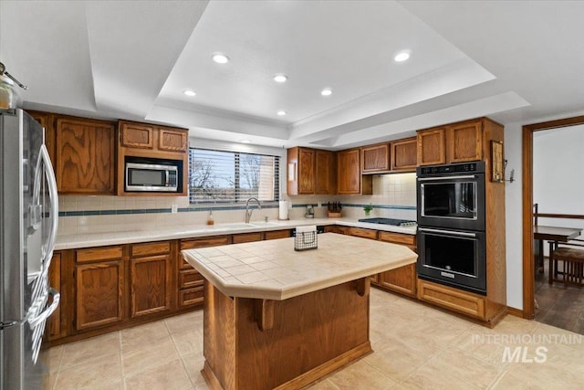 kitchen featuring a kitchen island, stainless steel appliances, backsplash, a raised ceiling, and tile countertops