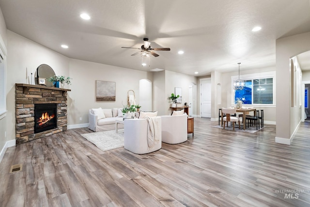 living area featuring wood finished floors, recessed lighting, a fireplace, arched walkways, and ceiling fan with notable chandelier