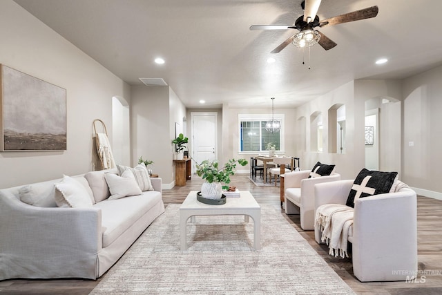 living room with visible vents, recessed lighting, arched walkways, light wood-style floors, and ceiling fan with notable chandelier