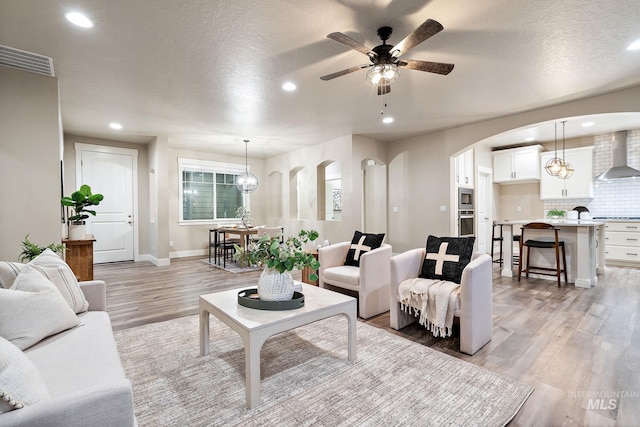 living area featuring a ceiling fan, a textured ceiling, recessed lighting, arched walkways, and light wood finished floors