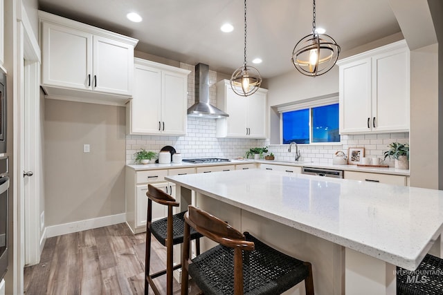 kitchen with a breakfast bar area, stainless steel appliances, light wood-style floors, wall chimney exhaust hood, and a center island