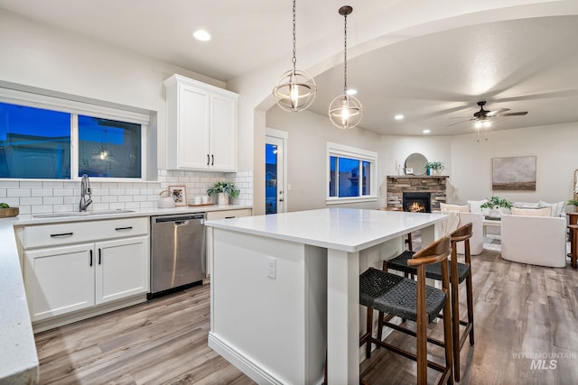 kitchen with a center island, light wood-type flooring, decorative backsplash, stainless steel dishwasher, and a sink