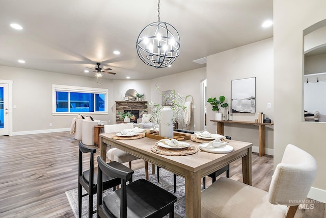 dining room featuring recessed lighting, ceiling fan with notable chandelier, a fireplace, and light wood-type flooring