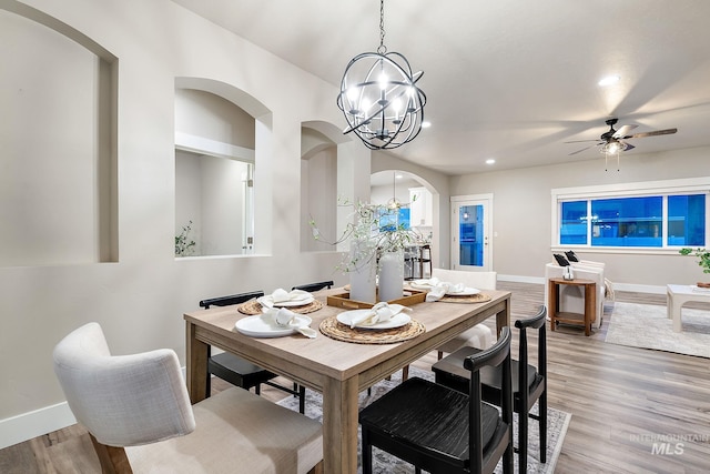 dining room with arched walkways, light wood-style flooring, ceiling fan with notable chandelier, and baseboards