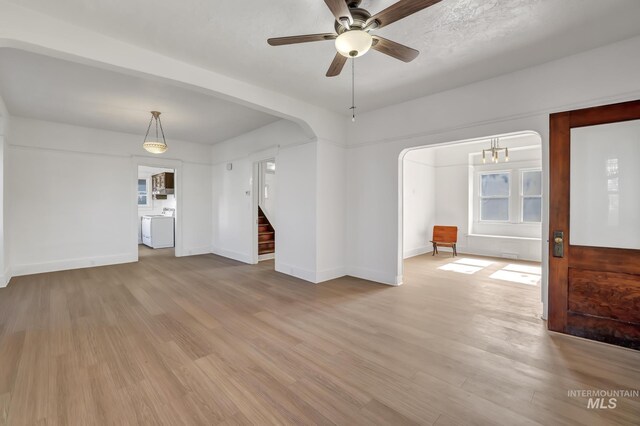 empty room with arched walkways, light wood finished floors, ceiling fan, baseboards, and stairs