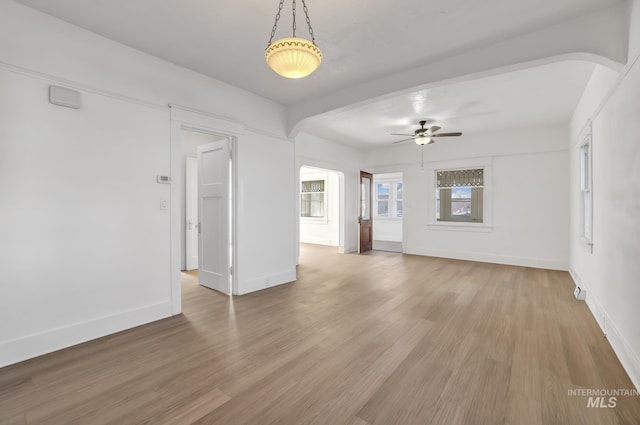 empty room featuring ceiling fan, light wood-type flooring, arched walkways, and baseboards