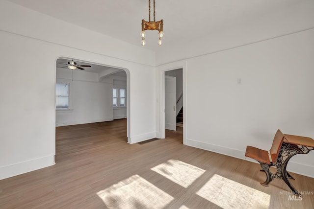 unfurnished dining area with arched walkways, light wood-style flooring, baseboards, stairway, and an inviting chandelier