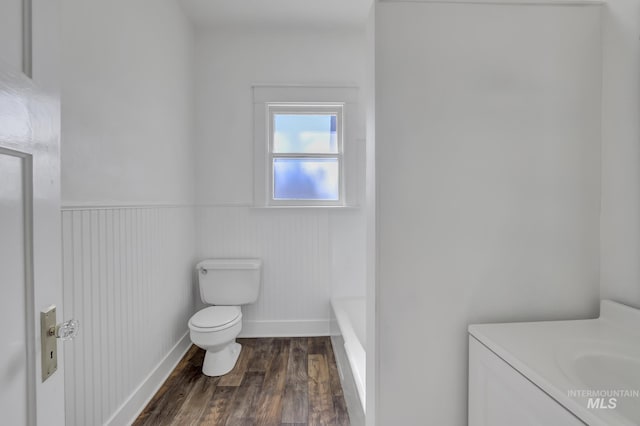 bathroom featuring a tub to relax in, toilet, wainscoting, vanity, and wood finished floors