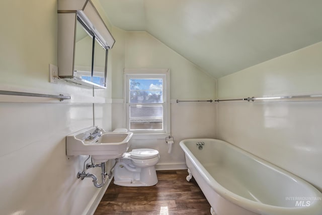 bathroom with lofted ceiling, toilet, wood finished floors, a freestanding tub, and a sink