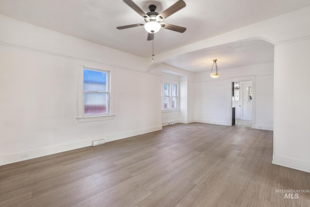 unfurnished room with ceiling fan, arched walkways, wood finished floors, and baseboards