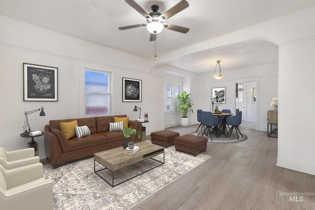 living room featuring a ceiling fan, arched walkways, baseboards, and light wood finished floors