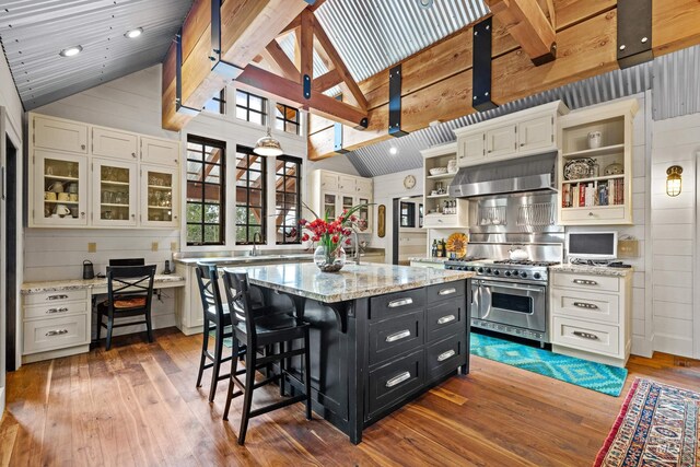 kitchen with double oven range, lofted ceiling with beams, sink, light stone countertops, and light wood-type flooring