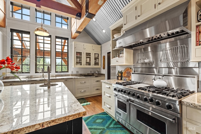 kitchen with exhaust hood, double oven range, light stone countertops, light wood finished floors, and glass insert cabinets