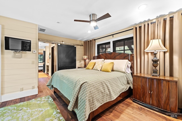 bedroom featuring a barn door, multiple windows, wood finished floors, and visible vents