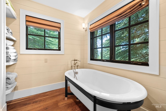 bathroom with a bath, plenty of natural light, wooden walls, and wood-type flooring