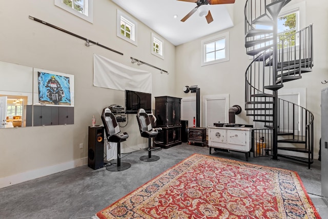 interior space with a towering ceiling, a wood stove, ceiling fan, concrete flooring, and baseboards