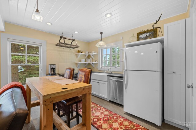 kitchen featuring dishwasher, freestanding refrigerator, hanging light fixtures, white cabinetry, and a sink