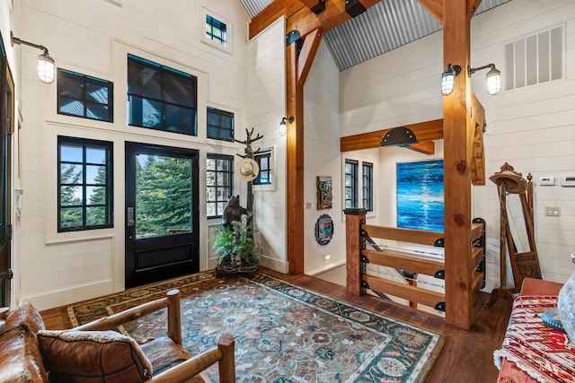 foyer entrance featuring a towering ceiling, wooden walls, visible vents, and dark wood-type flooring