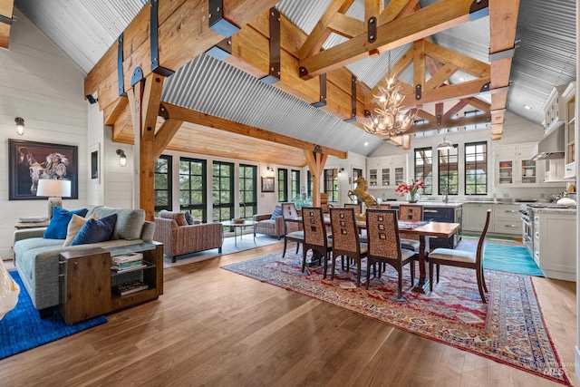 dining room featuring light wood-style floors, high vaulted ceiling, wooden walls, and an inviting chandelier