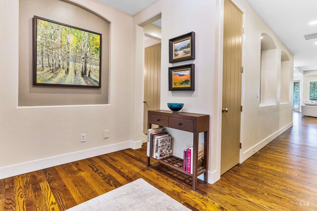 hallway featuring wood finished floors, baseboards, and arched walkways