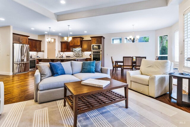 living room with a chandelier, wood finished floors, beverage cooler, recessed lighting, and baseboards