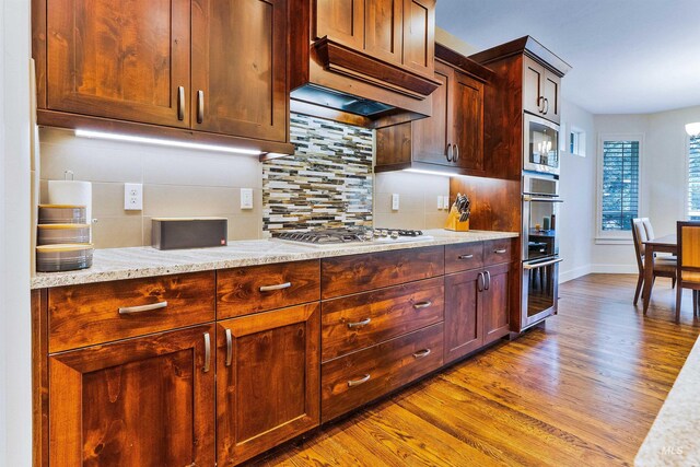 kitchen featuring appliances with stainless steel finishes, wood finished floors, decorative backsplash, baseboards, and light stone countertops