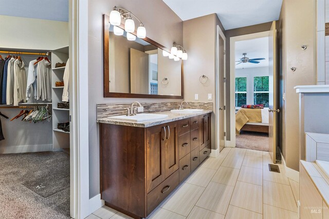 full bath with ensuite bath, double vanity, a spacious closet, a ceiling fan, and baseboards