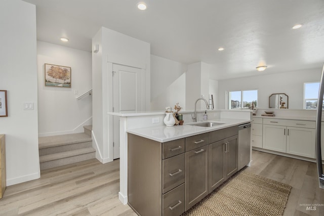 kitchen featuring sink, an island with sink, stainless steel dishwasher, and light wood-type flooring