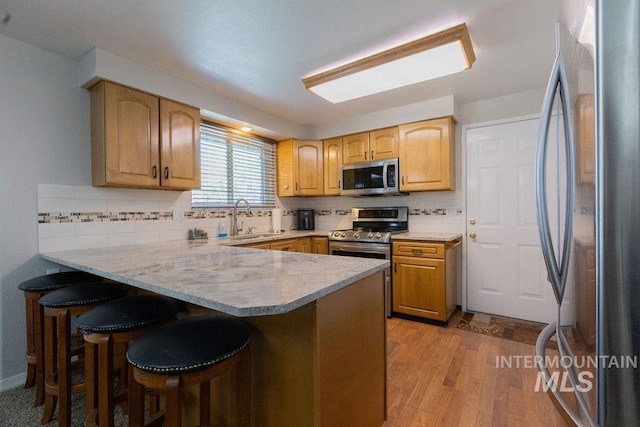 kitchen featuring a kitchen breakfast bar, a sink, appliances with stainless steel finishes, a peninsula, and backsplash