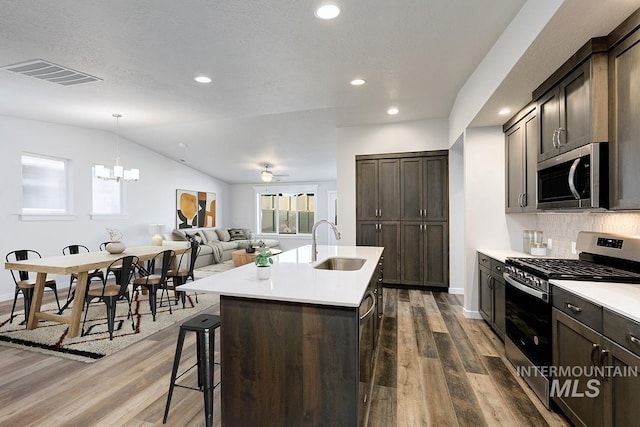 kitchen featuring stainless steel appliances, vaulted ceiling, a kitchen island with sink, sink, and pendant lighting