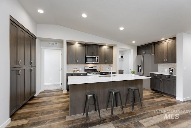 kitchen featuring appliances with stainless steel finishes, a breakfast bar, vaulted ceiling, sink, and an island with sink