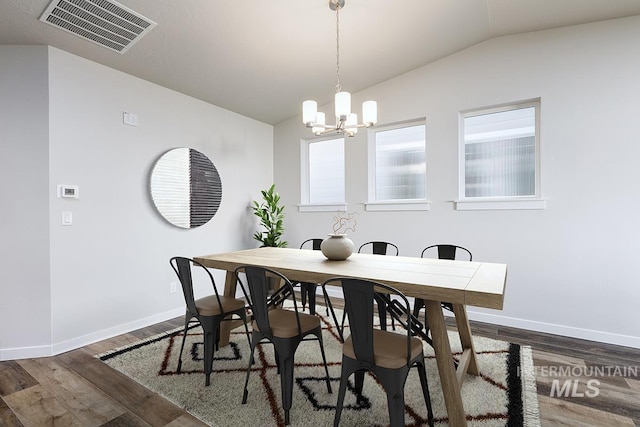 dining space with dark hardwood / wood-style floors, lofted ceiling, and an inviting chandelier