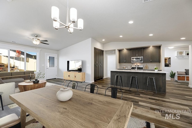 dining room with vaulted ceiling, ceiling fan with notable chandelier, and dark hardwood / wood-style floors