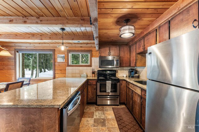 kitchen with kitchen peninsula, light stone counters, stainless steel appliances, hanging light fixtures, and wood walls