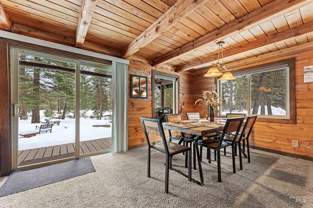 carpeted dining room with beam ceiling, wood walls, and wooden ceiling