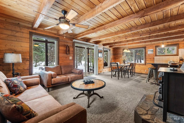 living room featuring beam ceiling, a wood stove, wood walls, and plenty of natural light