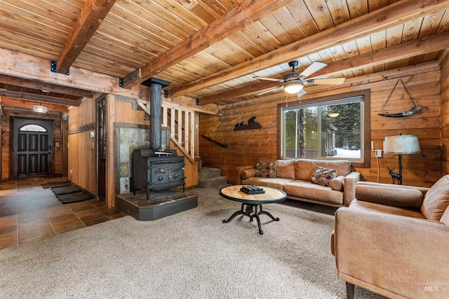 living room featuring beam ceiling, a wood stove, and wood walls