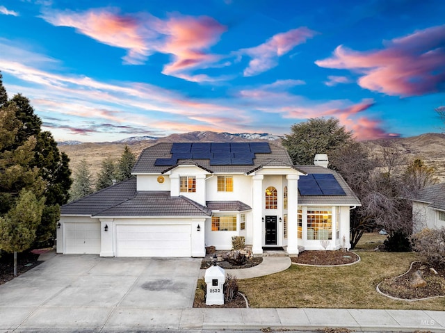 view of front facade with an attached garage, a tile roof, driveway, roof mounted solar panels, and a front yard