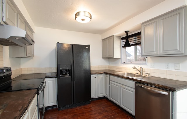 kitchen with a sink, under cabinet range hood, dark countertops, dark wood-style floors, and appliances with stainless steel finishes