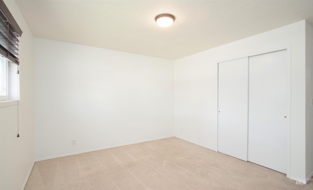 unfurnished bedroom featuring a closet, light colored carpet, and baseboards