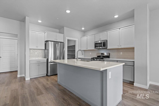 8450 S Bogus Ridge Ave, Boise, ID 83716 - kitchen featuring appliances with stainless steel finishes, a sink, decorative backsplash, a center island with sink, and wood finished floors