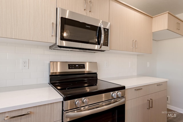 kitchen with light stone counters, light brown cabinets, stainless steel appliances, tasteful backsplash, and modern cabinets