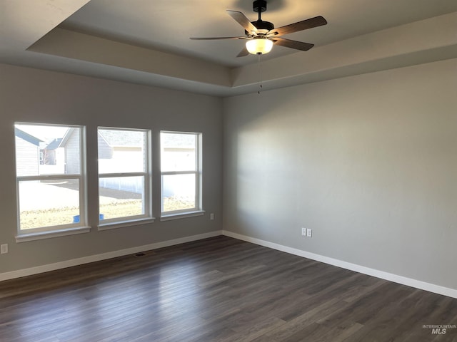 empty room featuring dark wood finished floors, a raised ceiling, and baseboards