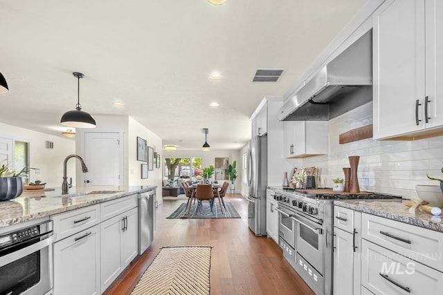kitchen with under cabinet range hood, a sink, white cabinetry, backsplash, and stainless steel appliances