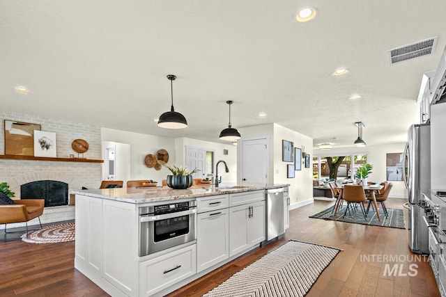 kitchen featuring visible vents, a sink, open floor plan, stainless steel appliances, and white cabinets
